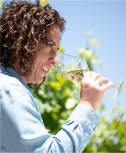 Seaglass winemaker Christine Morrison noses a glass of white wine standing in a sunny vineyard