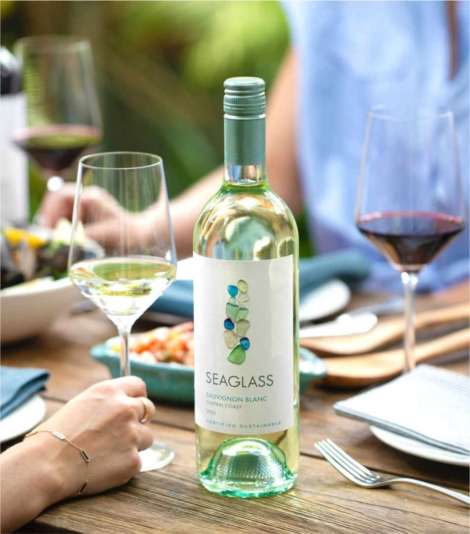 A bottle of Seaglass Central Coast Sauvignon Blanc white wine on a dinner table, with a hand holding a wine glass next to it