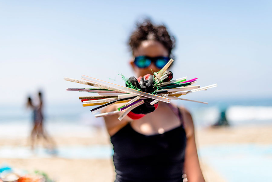 A person standing on a sunny beach holds pieces of colorful trash in their hand