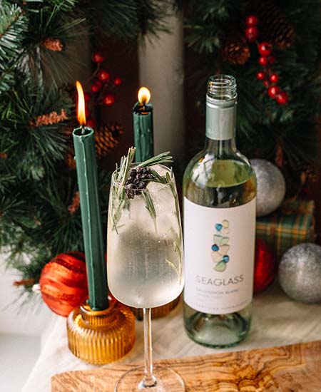Color image of a bottle of SEAGLASS Sauvignon Blanc next to a clear cocktail with holiday garnishes