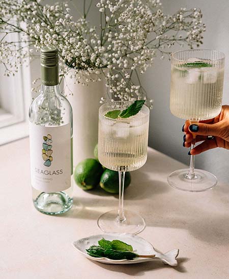 Two cocktails next to a bottle of SEAGLASS Pinot Grigio on a table next to a sunny window