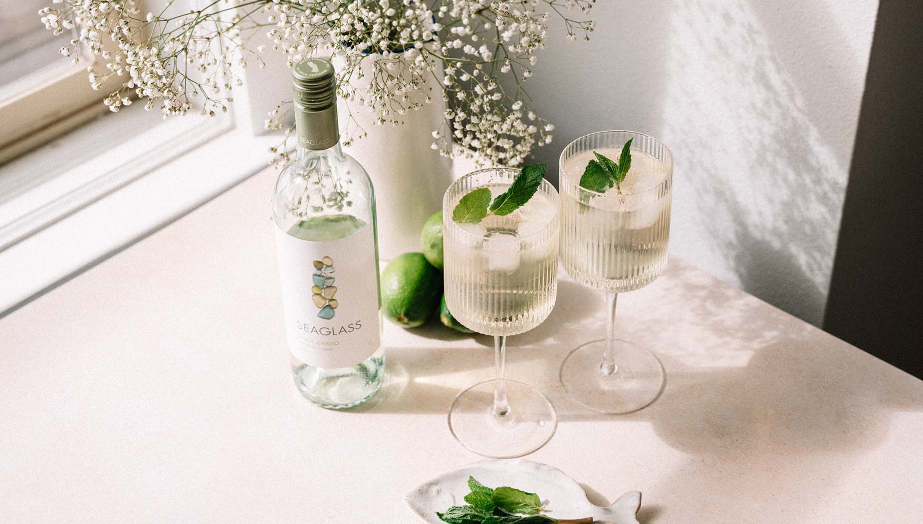 Two cocktails next to a bottle of SEAGLASS Pinot Grigio on a table next to a sunny window
