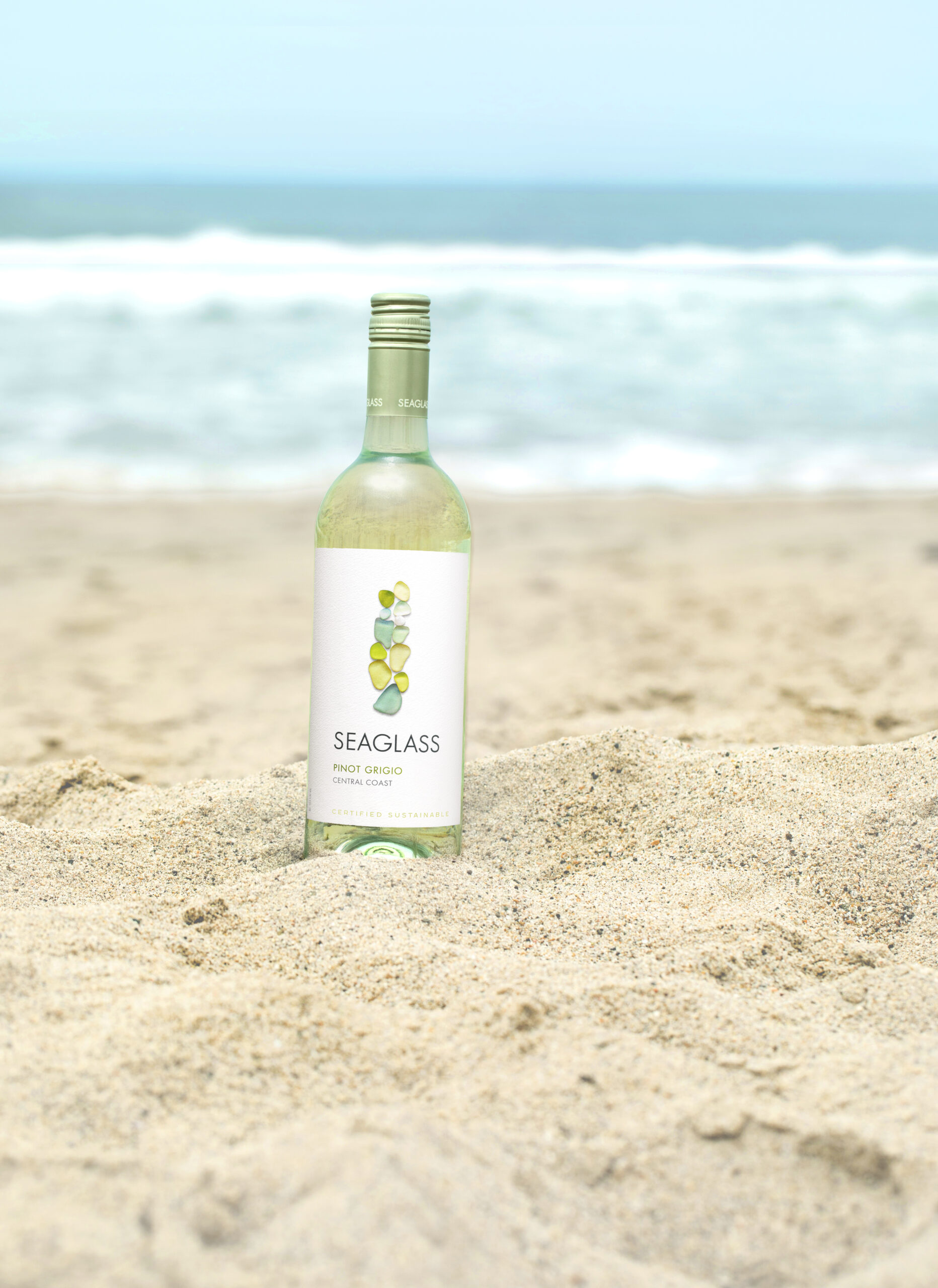 Seaglass Wine Co Pinot Grigio Wine bottle photo on the sand with the ocean in the background.