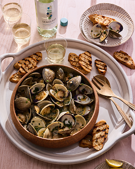 A bowl of Steamed Clams in White Wine + Herbs with a glass and bottle of SEAGLASS Sauvignon Blanc