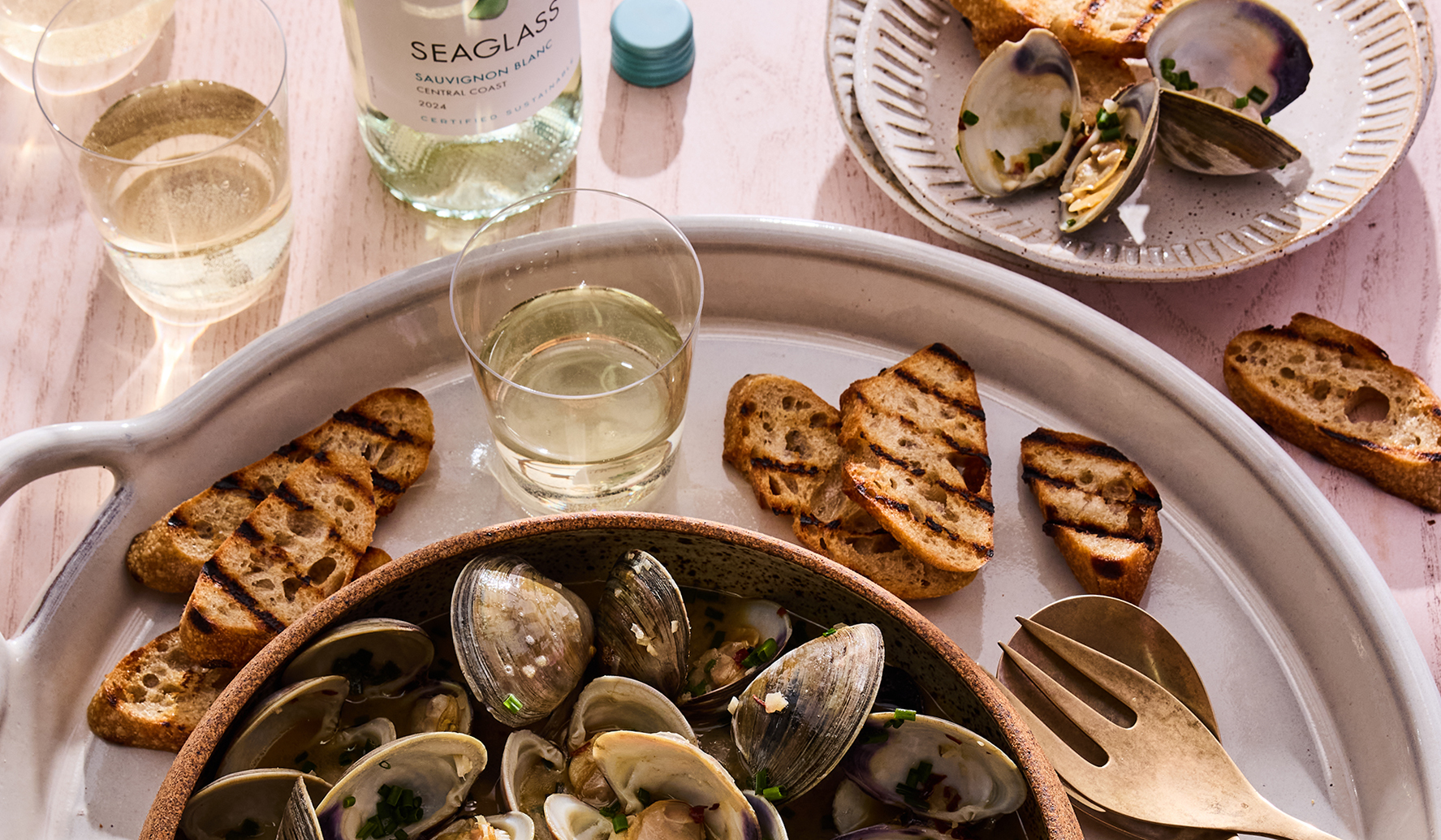 A bowl of Steamed Clams in White Wine + Herbs with a glass and bottle of SEAGLASS Sauvignon Blanc